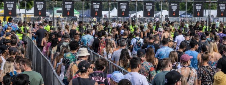 A large festival crowd queueing at a high-volume entry gate where barcode wristband throughput bottlenecks often lead to significant delays compared to RFID contactless systems. A large festival crowd queueing at a high-volume entry gate where barcode wristband throughput bottlenecks often lead to significant delays compared to RFID contactless systems.